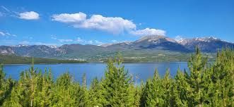 Lake with raft and people; surrounded by lush green trees and under a cloudy blue sky.