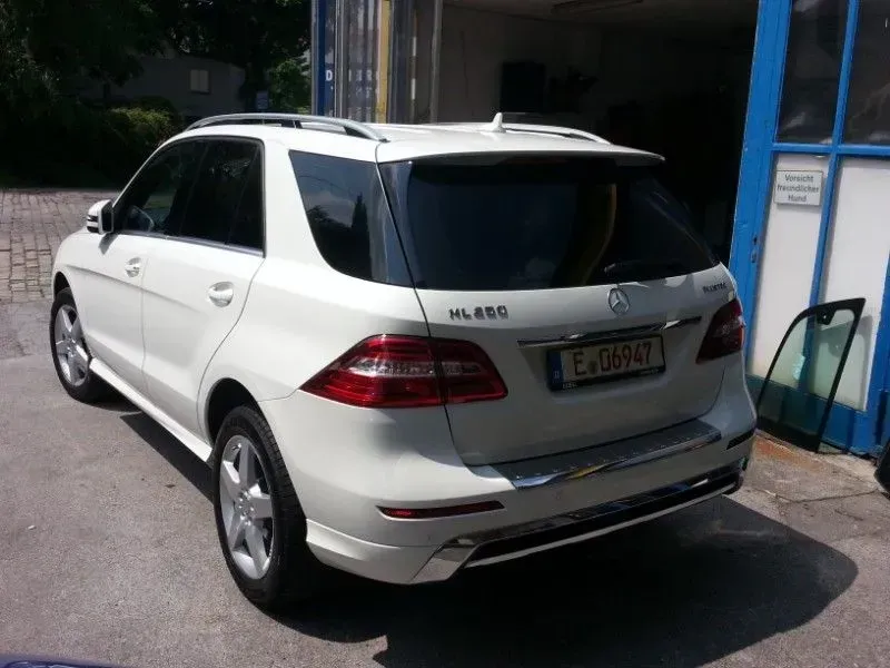 Weißer Mercedes-SUV, von hinten auf einer sonnigen Straße neben einem Gebäude geparkt.
