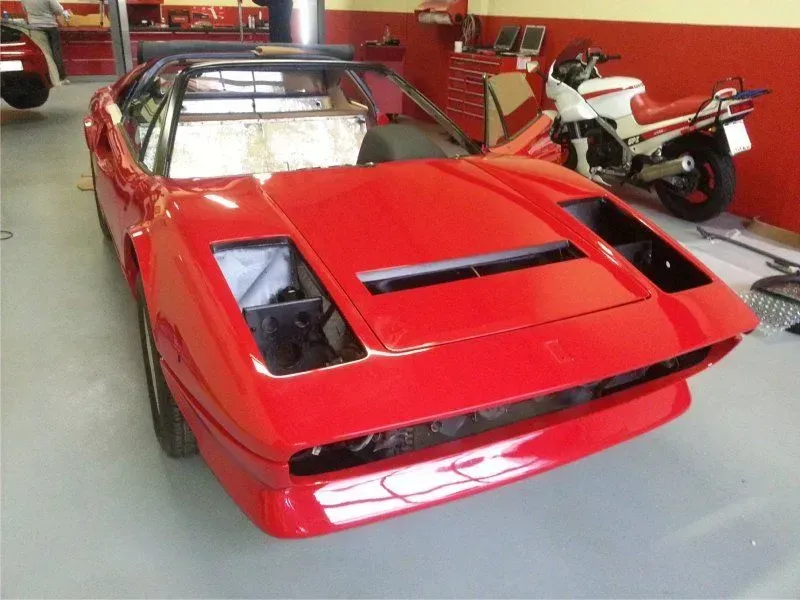 Roter Sportwagen in einer Garage, Ansicht von vorne links, mit einem weißen Motorrad im Hintergrund.