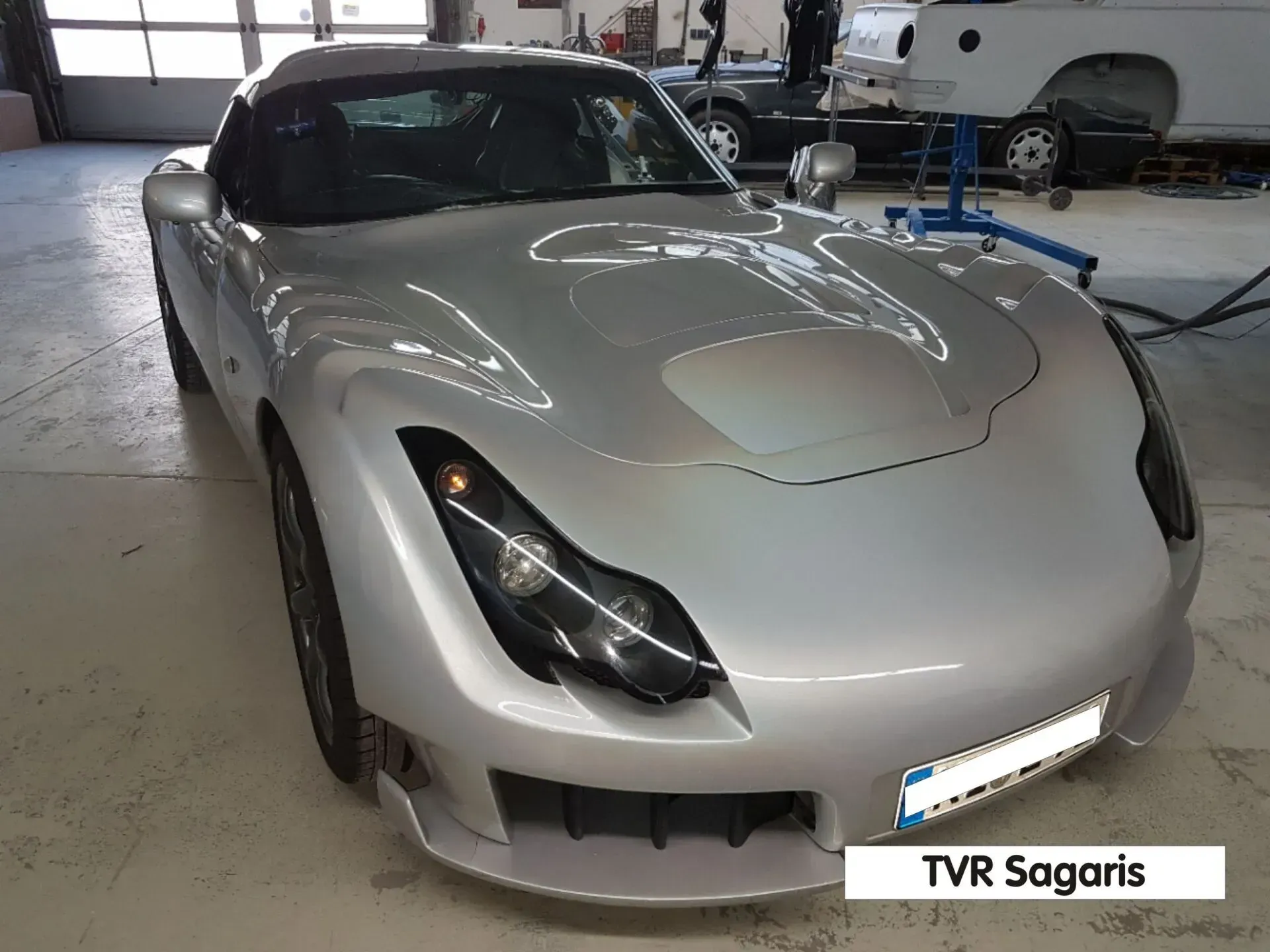 Silberner Sportwagen in einer Garage, Frontansicht mit Scheinwerfern und TVR-Sagaris-Kennzeichen.