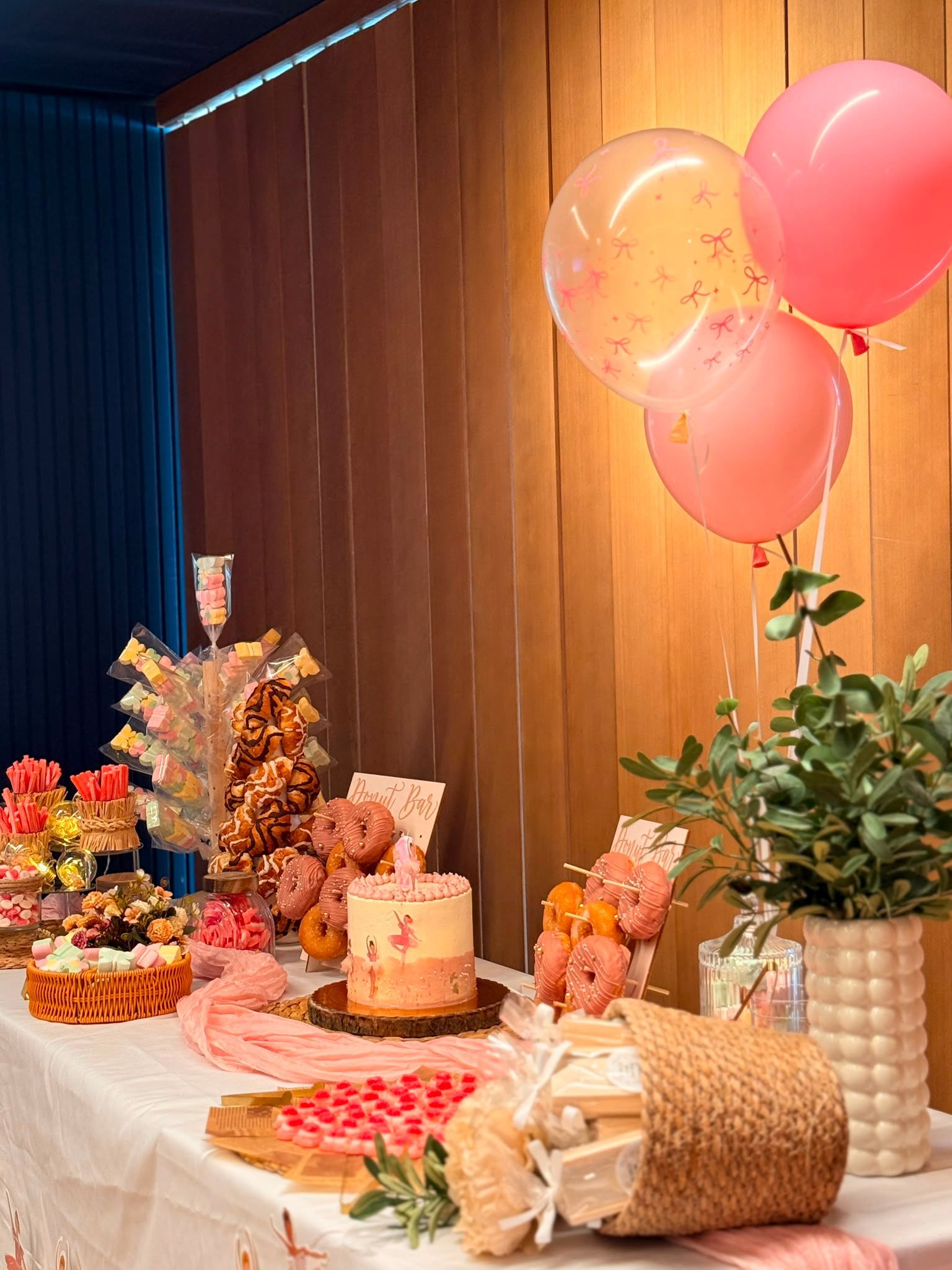 Mesa de postres decorada con globos, flores y pasteles sobre un fondo de paneles de madera.