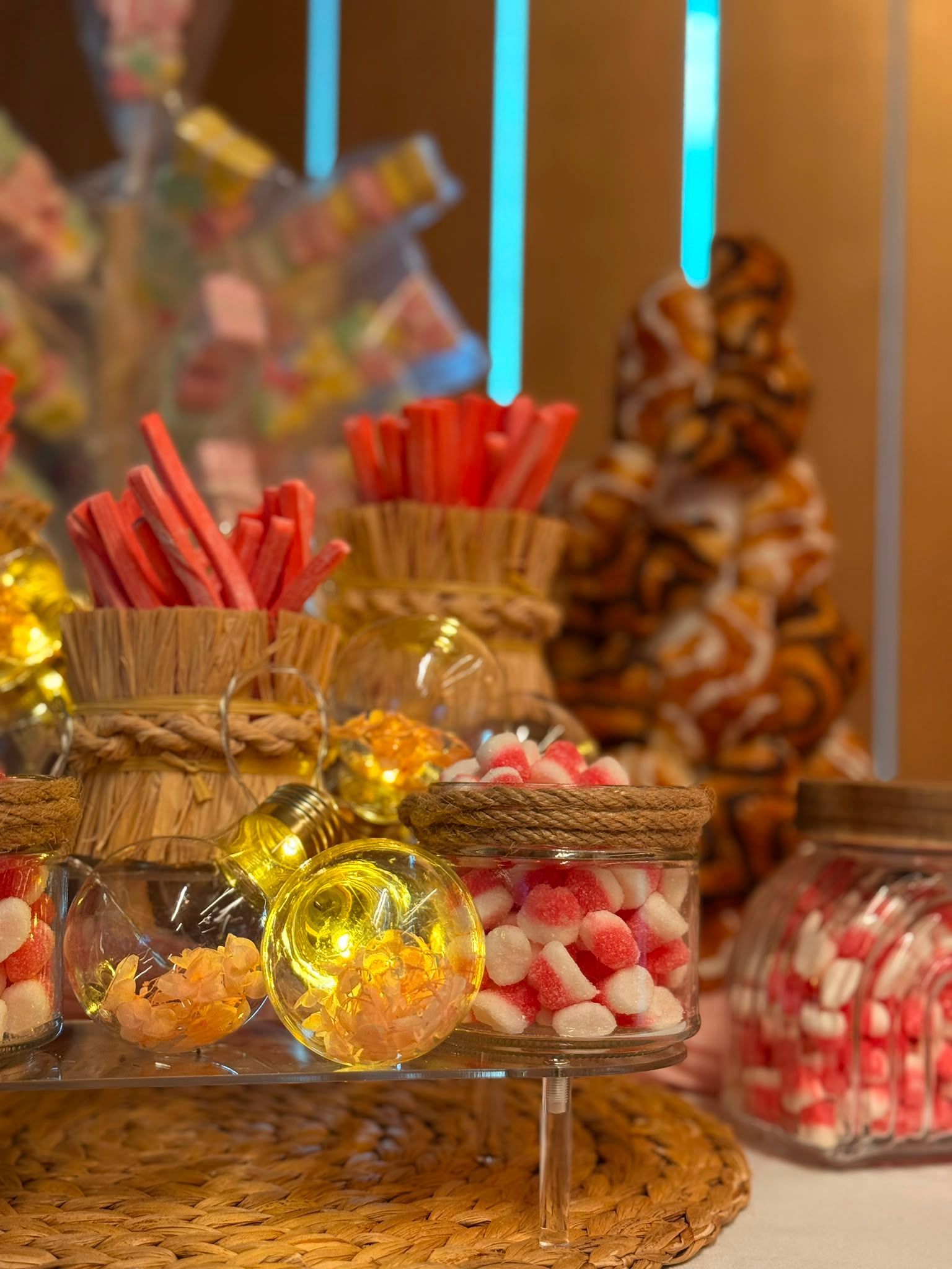 Exhibición de dulces con frascos de caramelos rojos, piruletas doradas y golosinas empaquetadas sobre una mesa festiva.