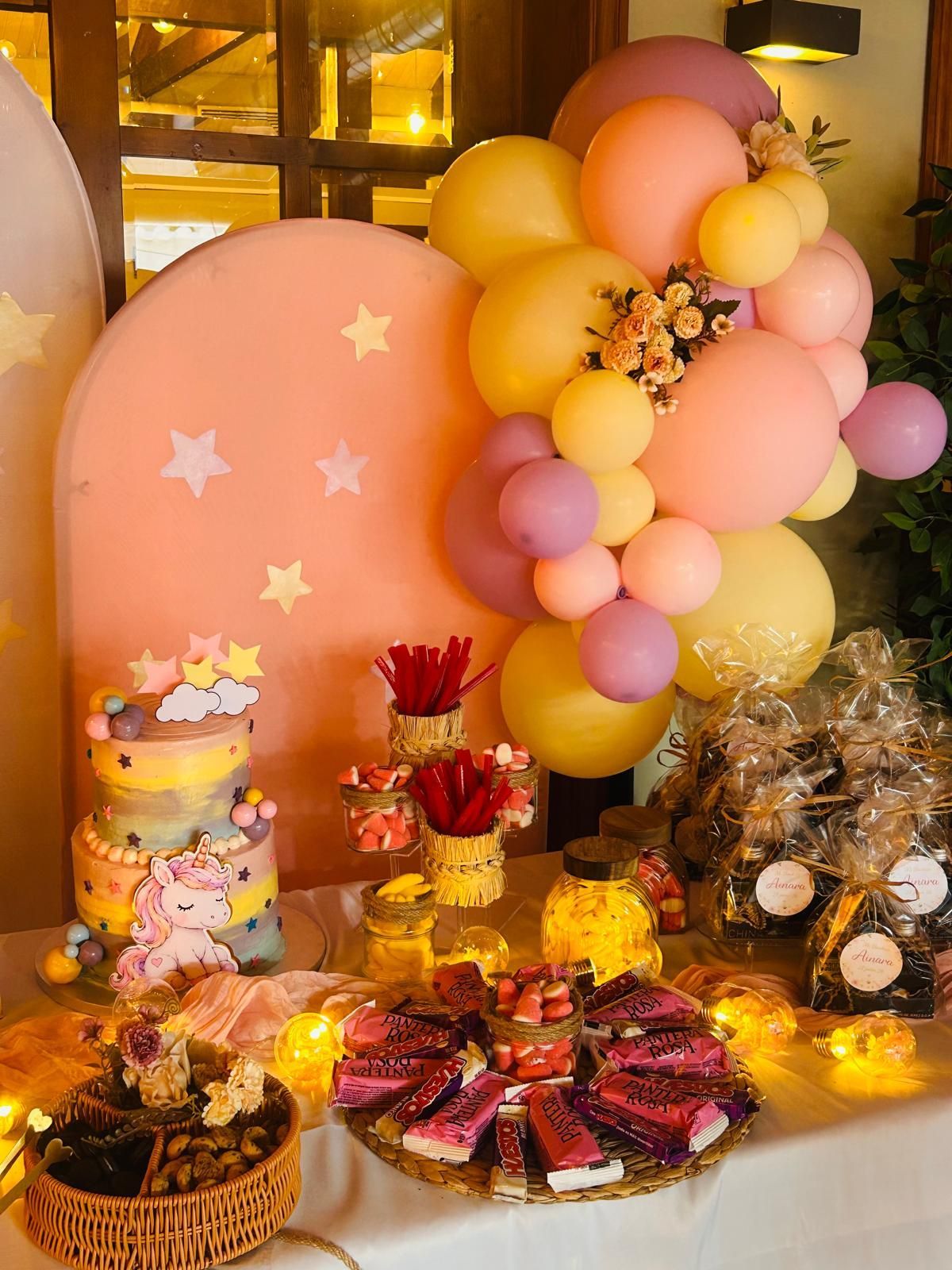 Decoración de fiesta con globos en tonos pastel, fondo de estrellas rosas y postres variados sobre una mesa decorada.
