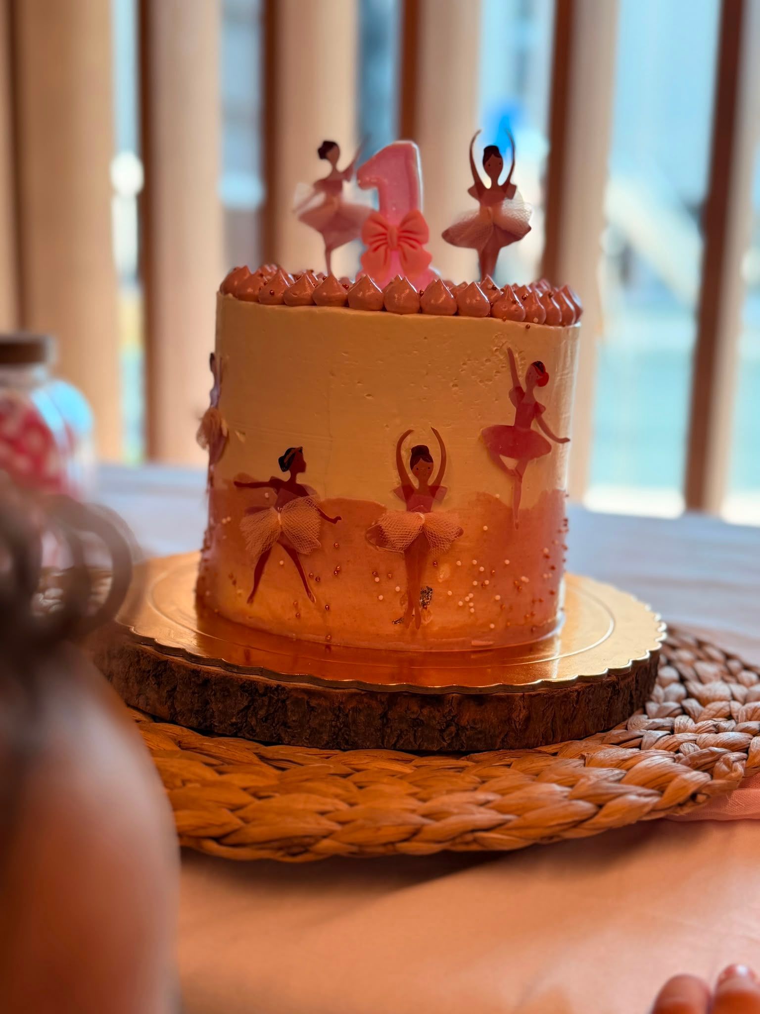 Adorno de bailarina rosa sobre una tarta de cumpleaños en tonos pastel, colocada sobre un mantel individual tejido