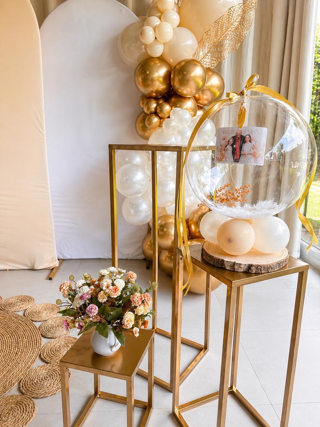 Elegante decoración con globos dorados y blancos, arreglos florales y soportes transparentes para globos 