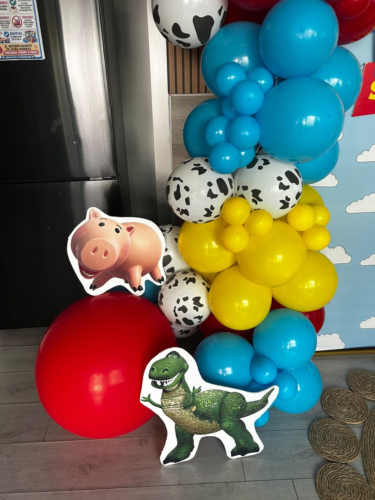 Columna de globos coloridos con recortes de dinosaurios, cerdos y vacas en una habitación, además de un gran globo rojo.