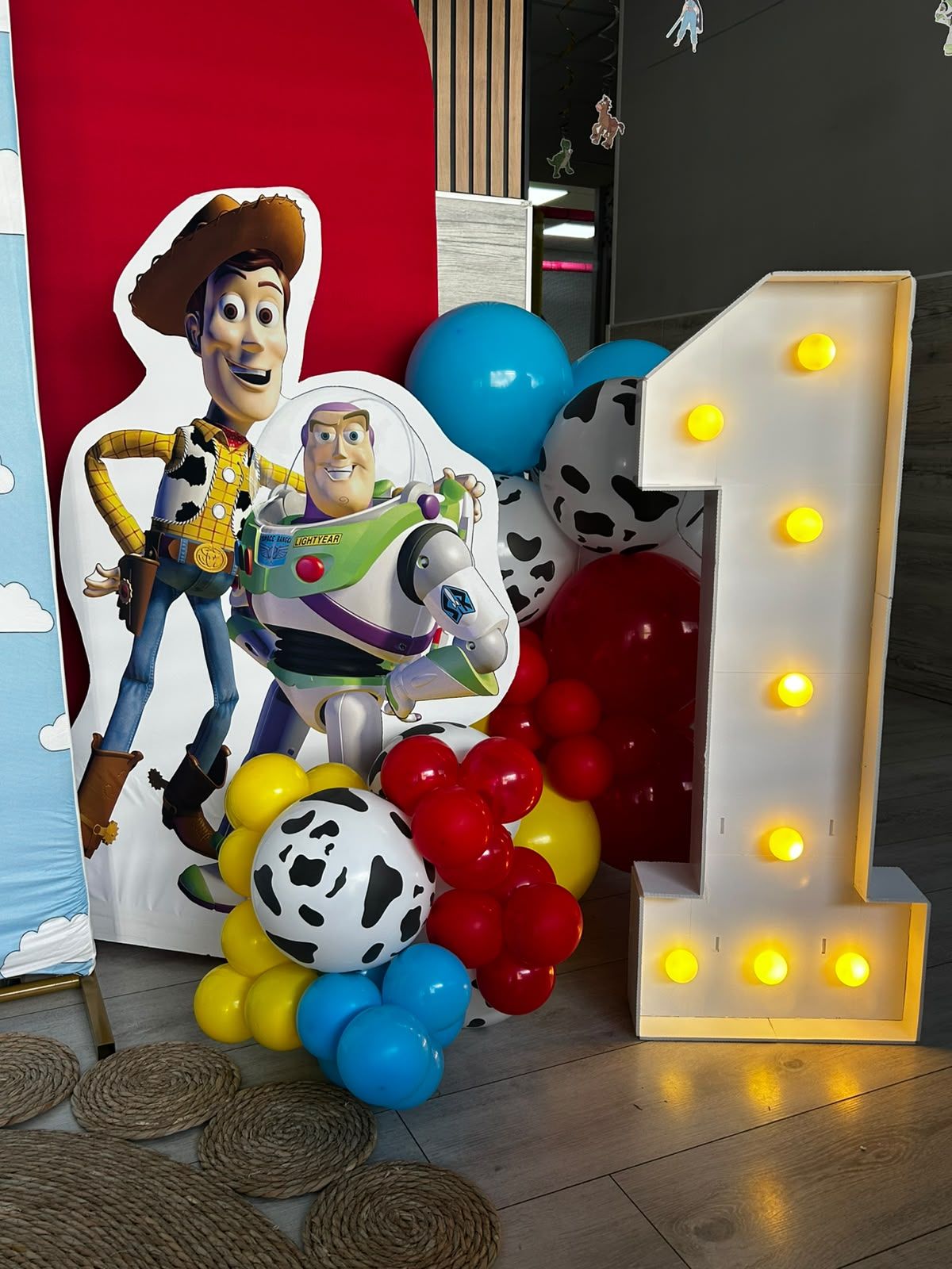 Decoración con personajes de Toy Story: globos de Woody y Buzz, globos rojos y azules, y un letrero luminoso con el número 1.