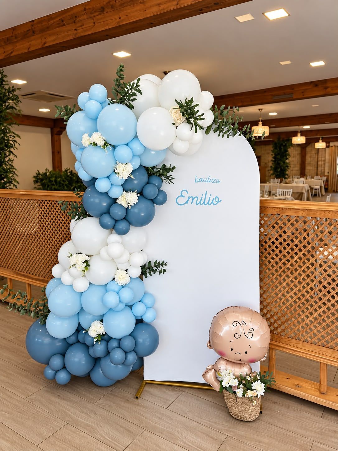 Exhibición de globos azules y blancos junto a un letrero en la entrada de una celebración en el interior, con una pequeña figura de globo debajo.