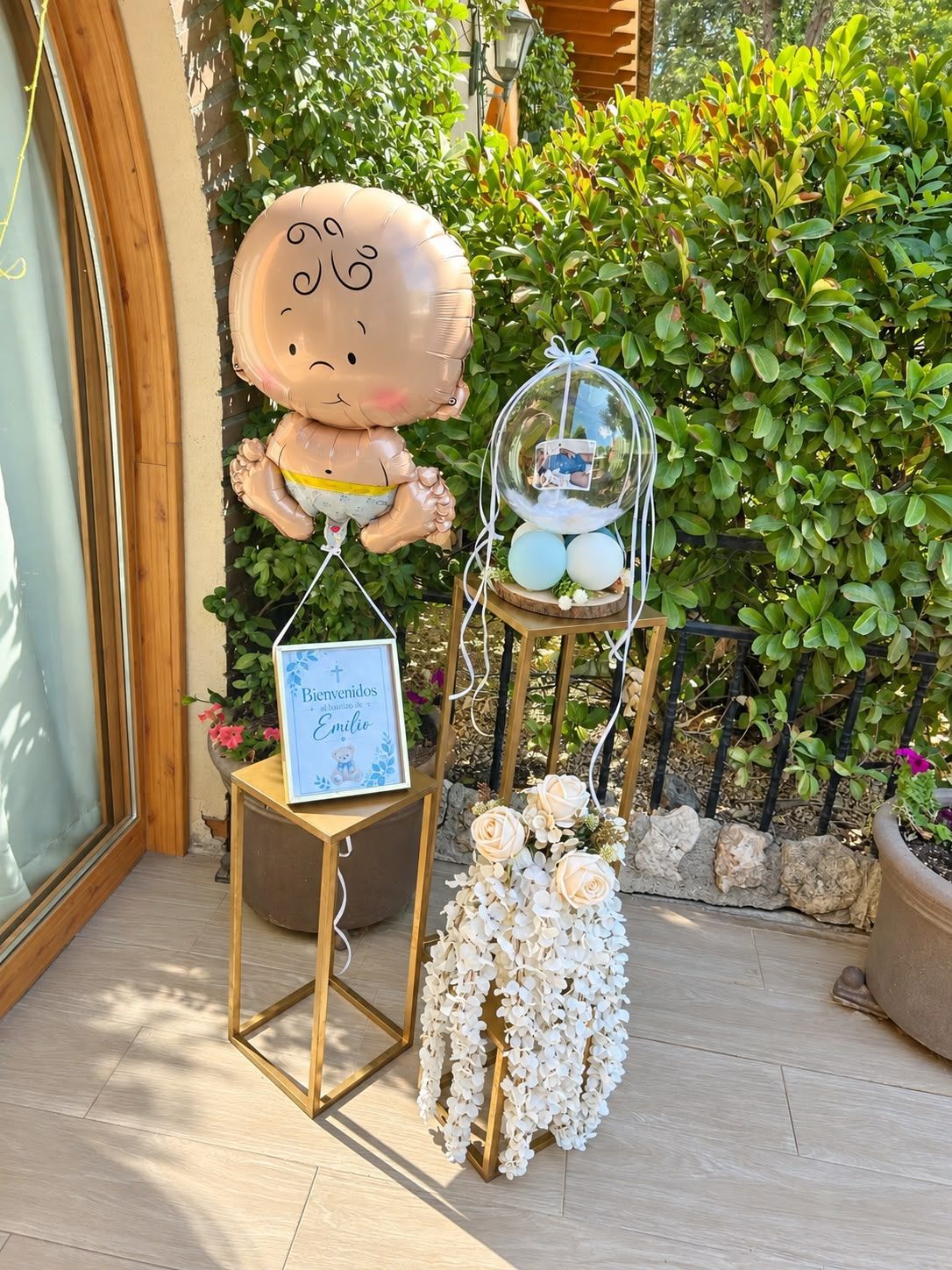 Exhibición exterior decorada con figuras de peluche, flores y un letrero enmarcado junto a una puerta de cristal.