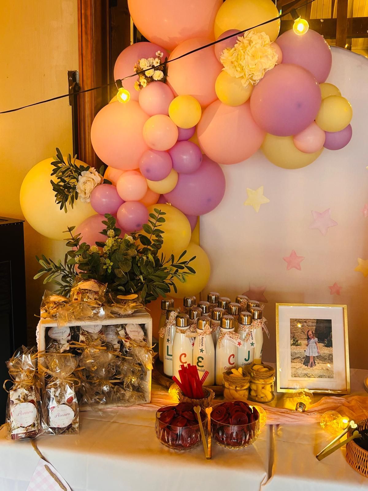 Arco de globos en tonos pastel sobre una mesa de fiesta decorada con detalles dorados y cajas de regalo.