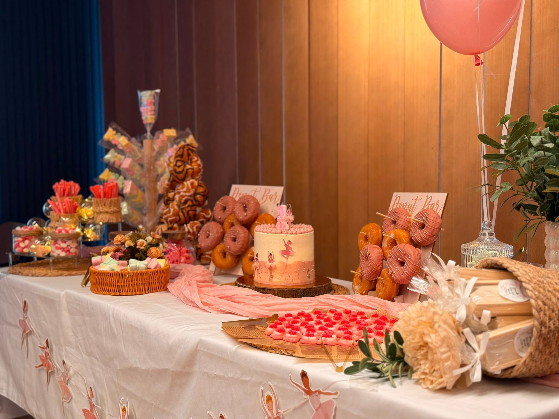 Mesa de postres decorada con pasteles, donas, bollería, flores y globos en una fiesta.