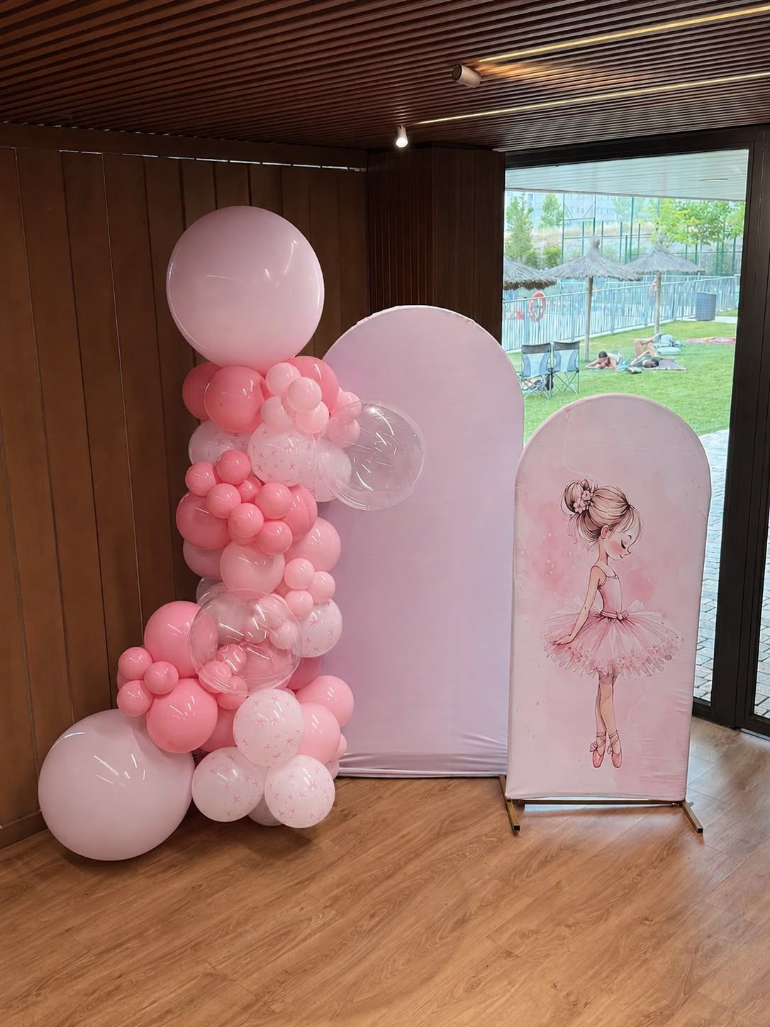 Arreglo floral con globos rosas junto a un soporte para flores en la entrada de un evento en el interior