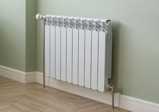 A white radiator is sitting on a wooden floor next to a green wall.