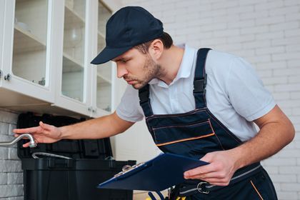 A man is holding a clipboard and looking at a hook in a kitchen.