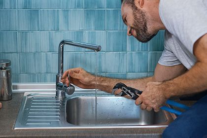 A man is fixing a faucet in a kitchen sink with a wrench.