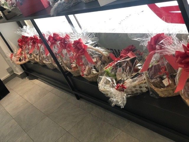 Cesti regalo avvolti in plastica trasparente con nastri rossi esposti sul pavimento di un negozio.