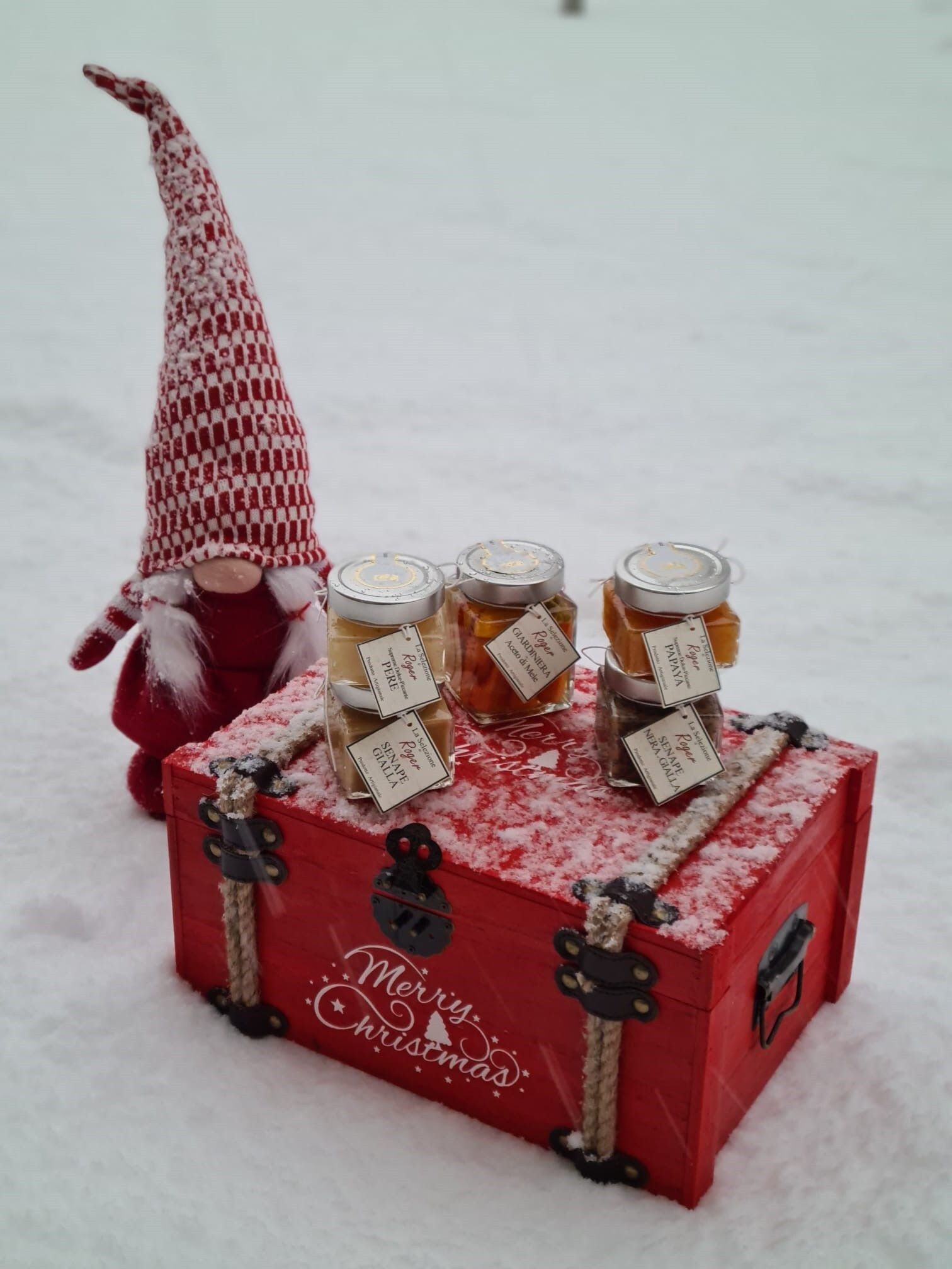 Scatola regalo rossa con tre vasetti e una piccola decorazione a forma di gnomo di Babbo Natale sulla parte superiore.