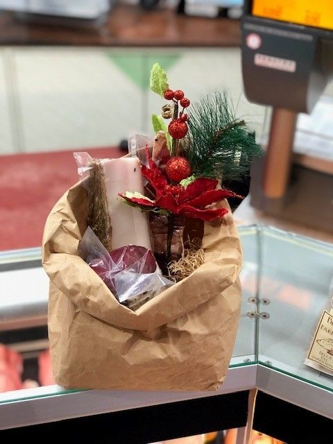 Sacchetto regalo di carta marrone con decorazioni natalizie rosse e articoli incartati su un bancone di vetro.