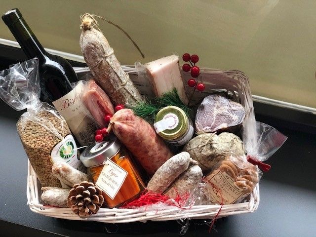 Cesto regalo con un assortimento di formaggi, salumi, pane, uva e una bottiglia di vino.