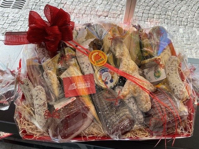 Cesto regalo con dolcetti assortiti confezionati in cellophane trasparente e un fiocco di nastro rosso.