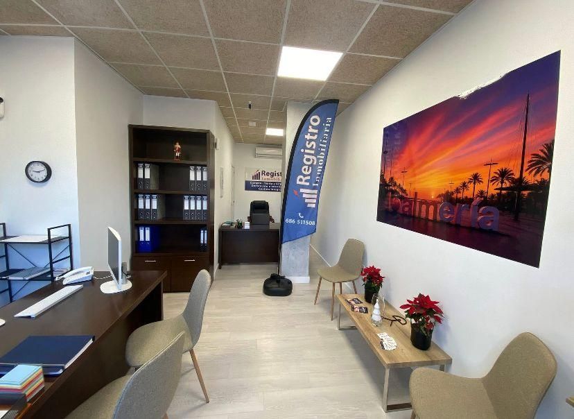 Interior de una oficina: escritorio, sillas, un póster del atardecer y una estantería con carpetas.