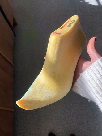 Un zapato amarillo en la horma, sostenido por una persona con un suéter blanco, en el interior.