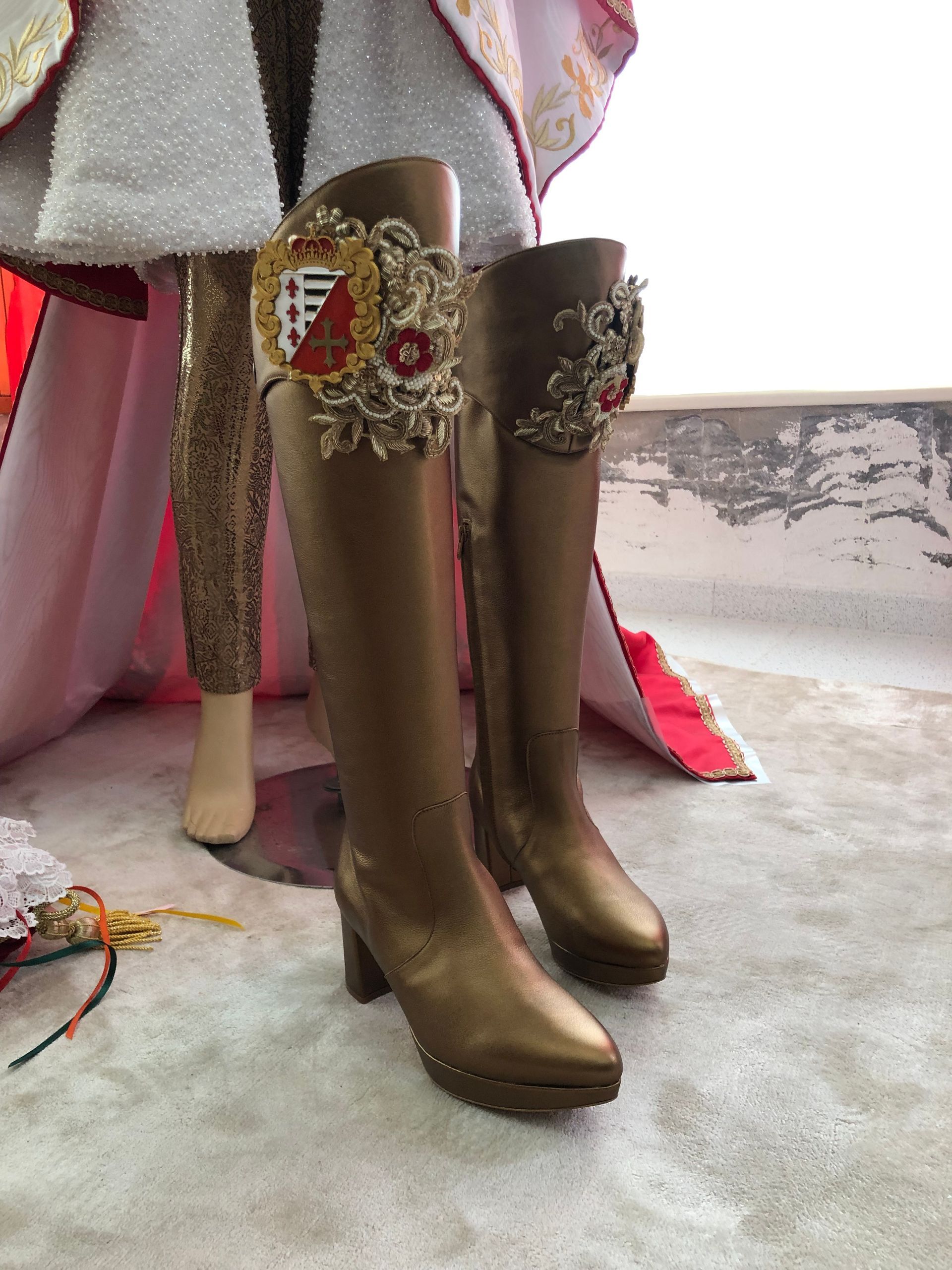 Botas doradas con crestas, parte de un elaborado disfraz de muñeca, sobre una superficie estampada.