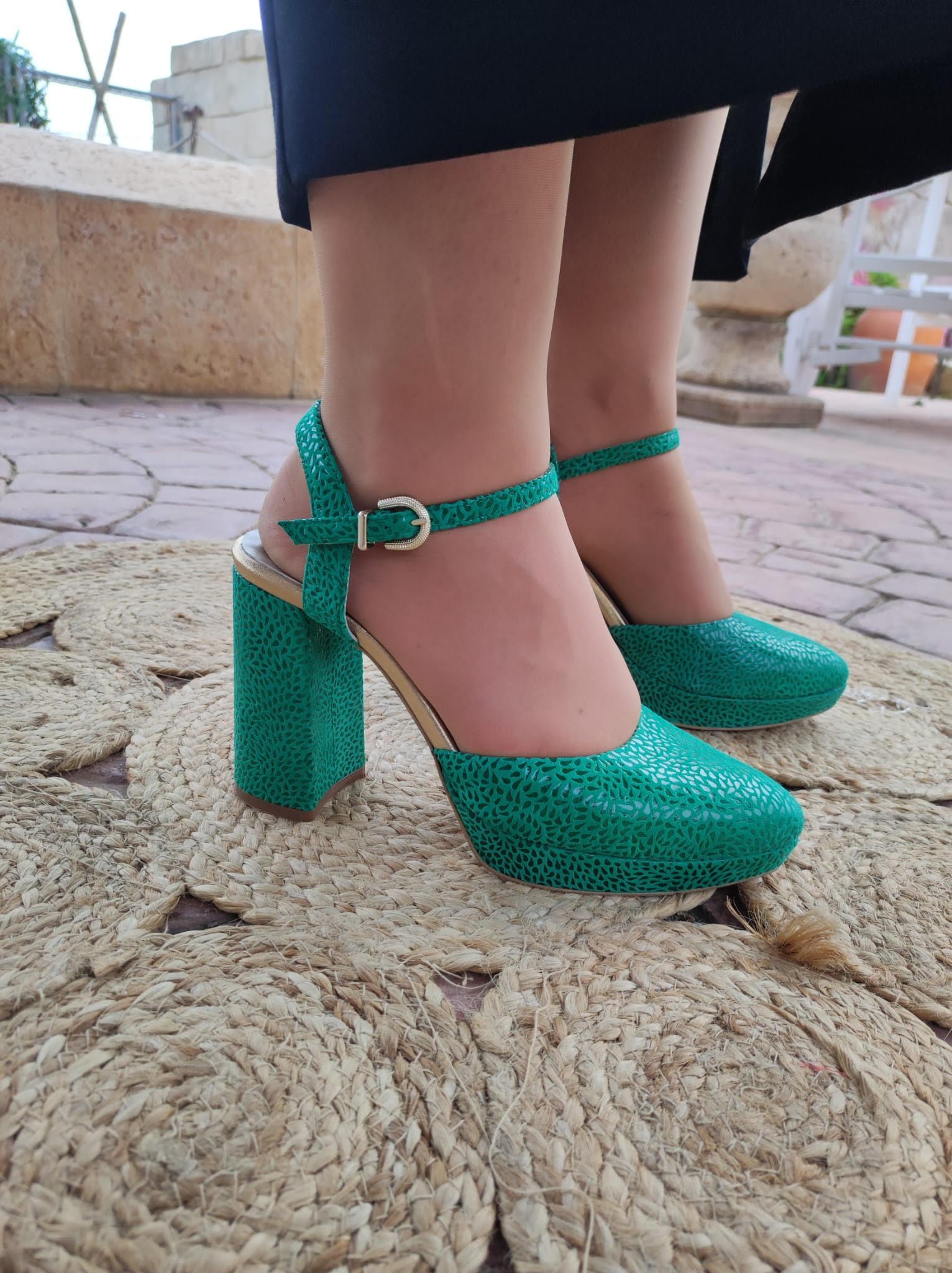 Zapatos verdes de tacón alto con tiras en el tobillo sobre una alfombra texturizada.