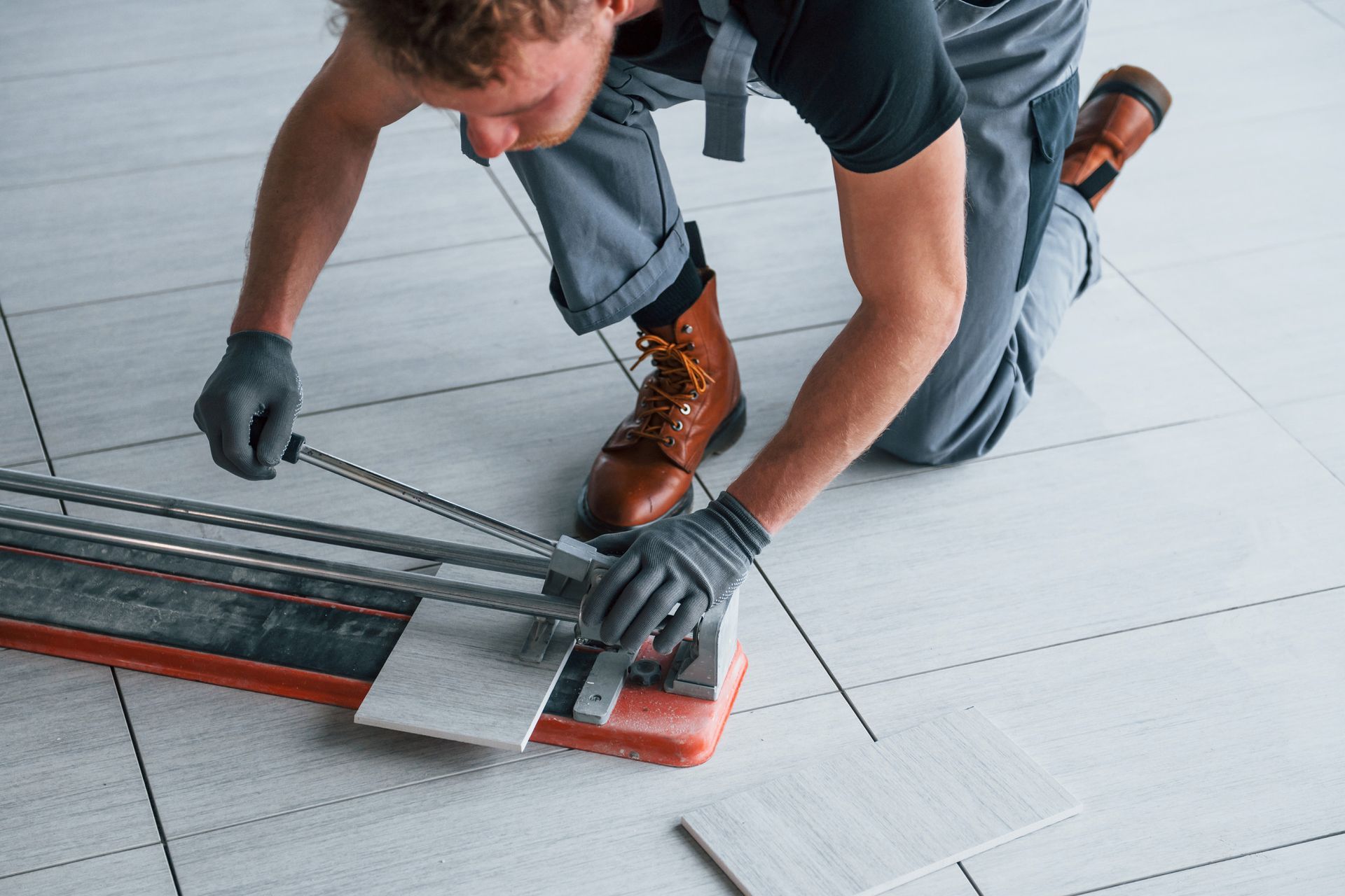 Persona arrodillada, cortando una baldosa con un cortador de baldosas en un suelo.