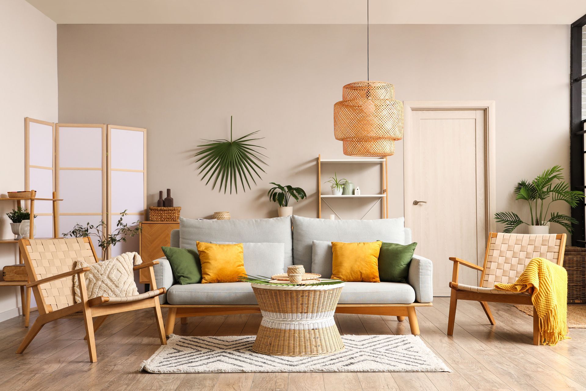 Sala de estar con muebles de colores claros, alfombra, plantas y lámpara tejida, con paredes beige y pisos de madera.