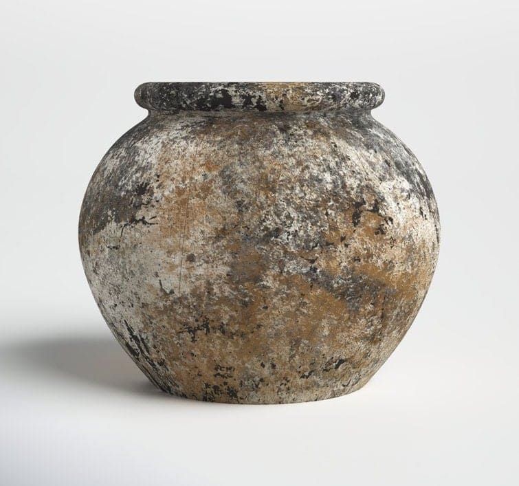Una maceta redonda de cerámica, desgastada por el tiempo, con un acabado texturizado y moteado en tonos marrones y grises, sobre un fondo blanco liso.