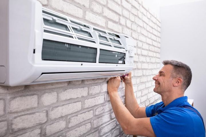 Un technicien installe un climatiseur mural sur un mur de briques, souriant et ajustant l'appareil.
