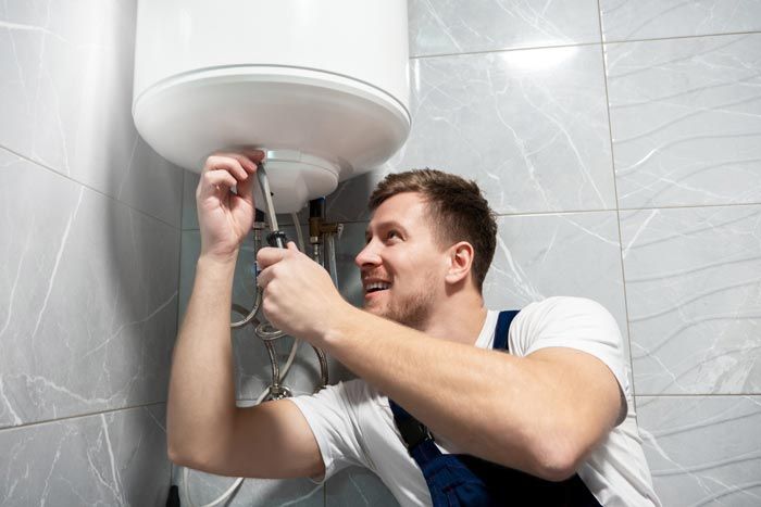 Un homme resserre un tuyau sous un lavabo blanc dans une salle de bains carrelée