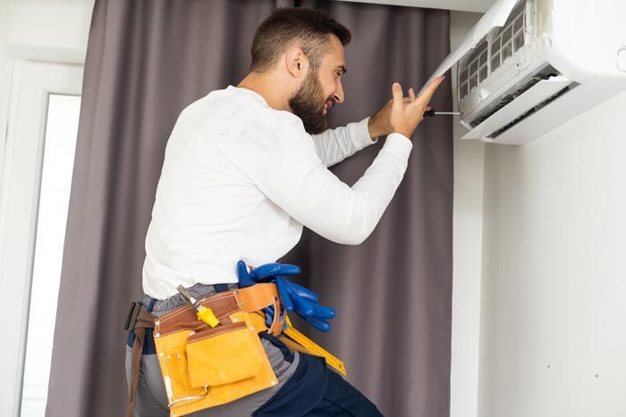 Un technicien inspecte un climatiseur mural avec ses outils à la ceinture.