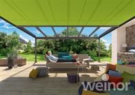 Ein Mann liegt auf einer Couch unter einer grünen Markise auf einer Terrasse.