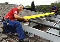 Ein Mann sitzt auf dem Dach eines Gebäudes und arbeitet an einem Solarpanel.