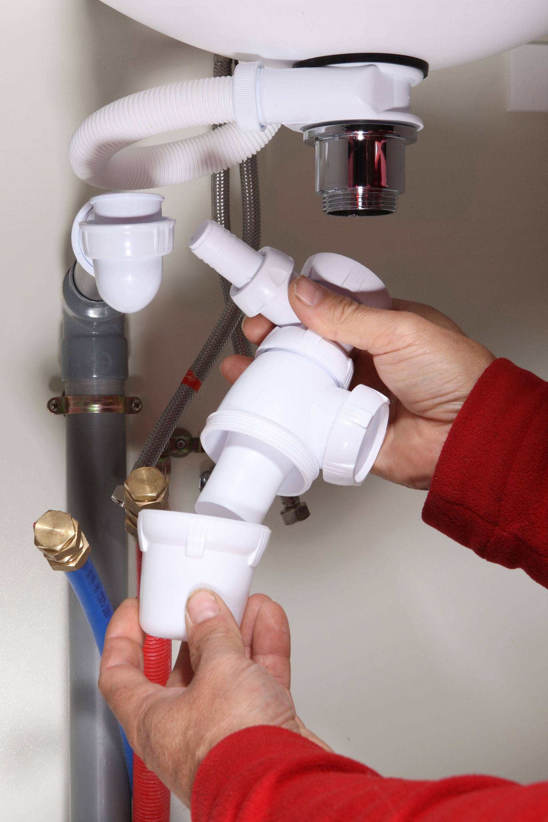 Des mains assemblent un tuyau d'évacuation d'évier en plastique blanc sous un évier blanc.