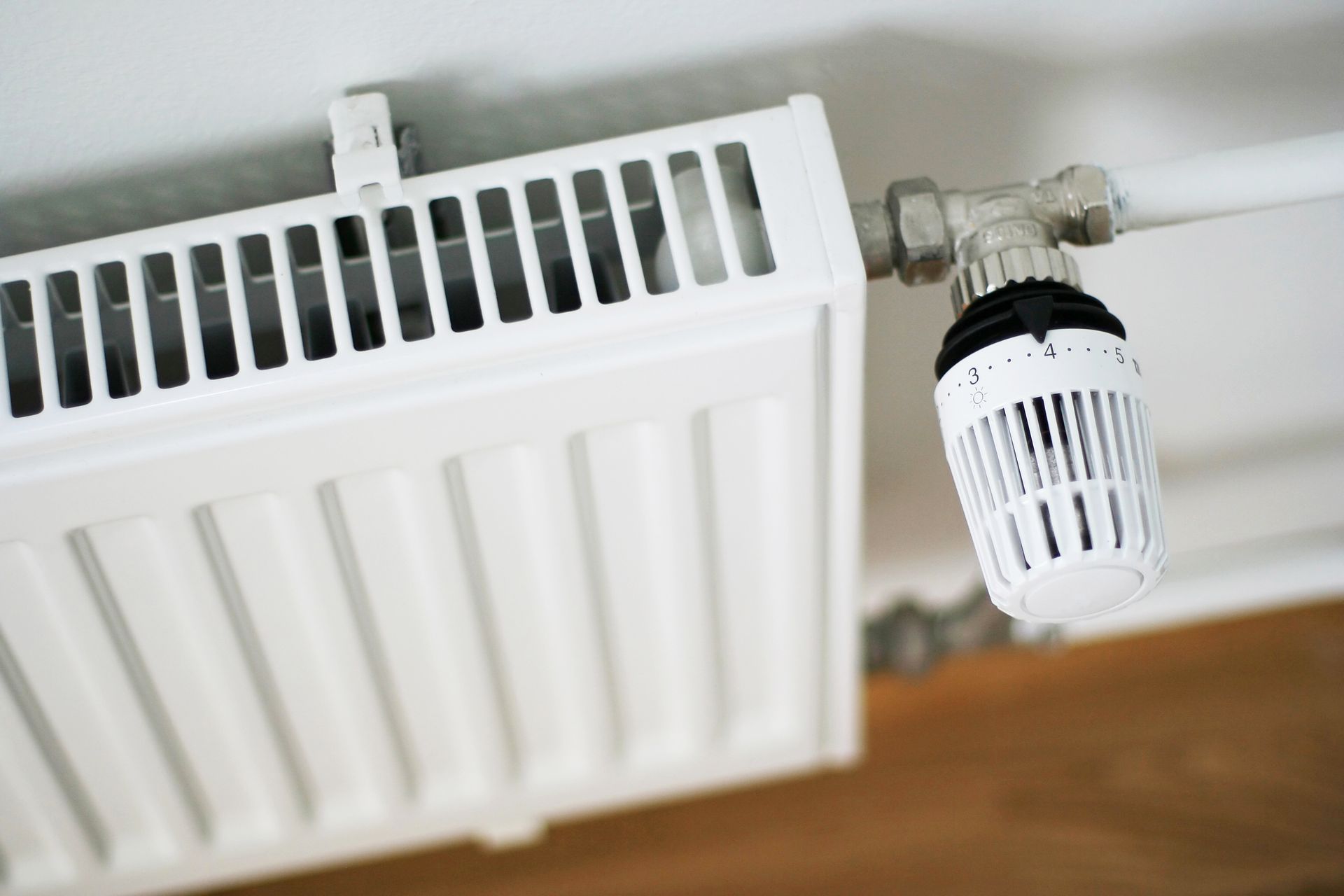 Radiateur blanc avec robinet thermostatique fixé à un tuyau blanc contre un mur blanc.