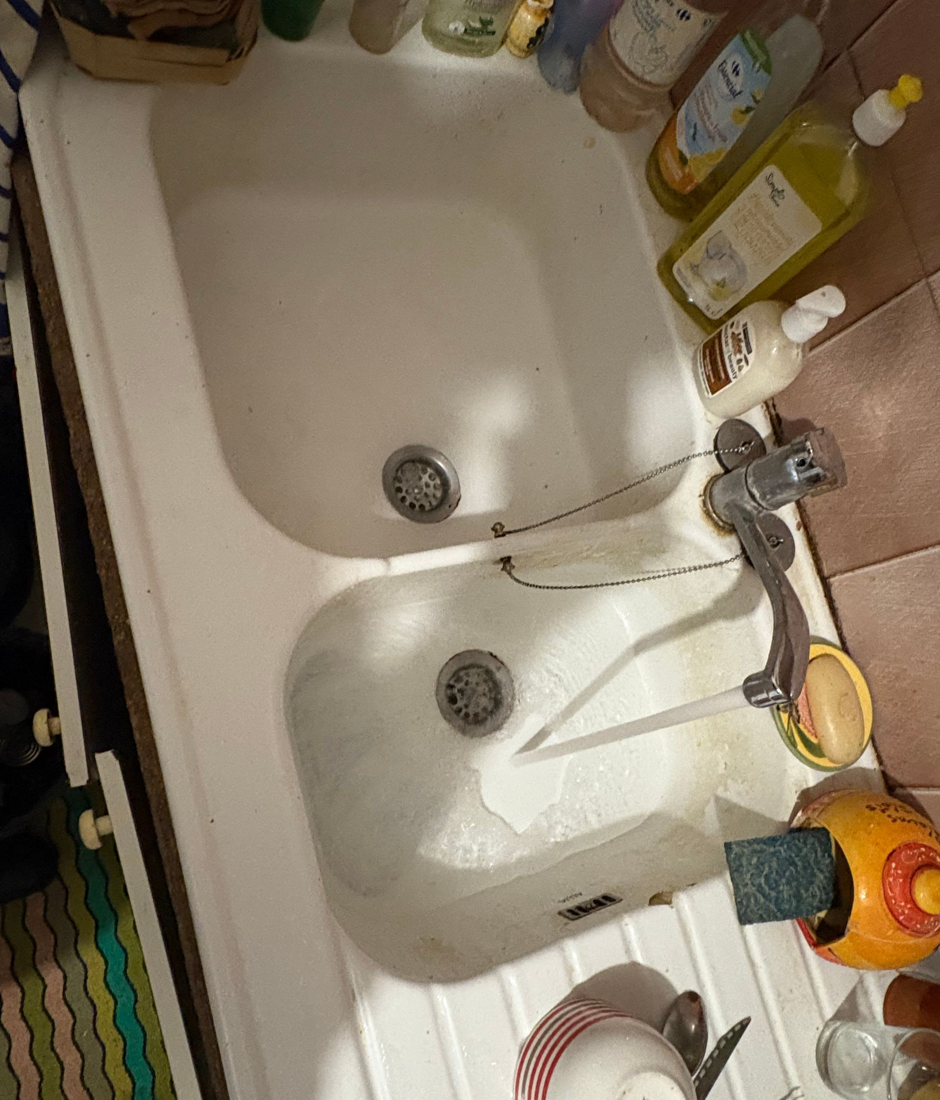 Évier double blanc avec eau courante ; divers produits de nettoyage l'entourent.