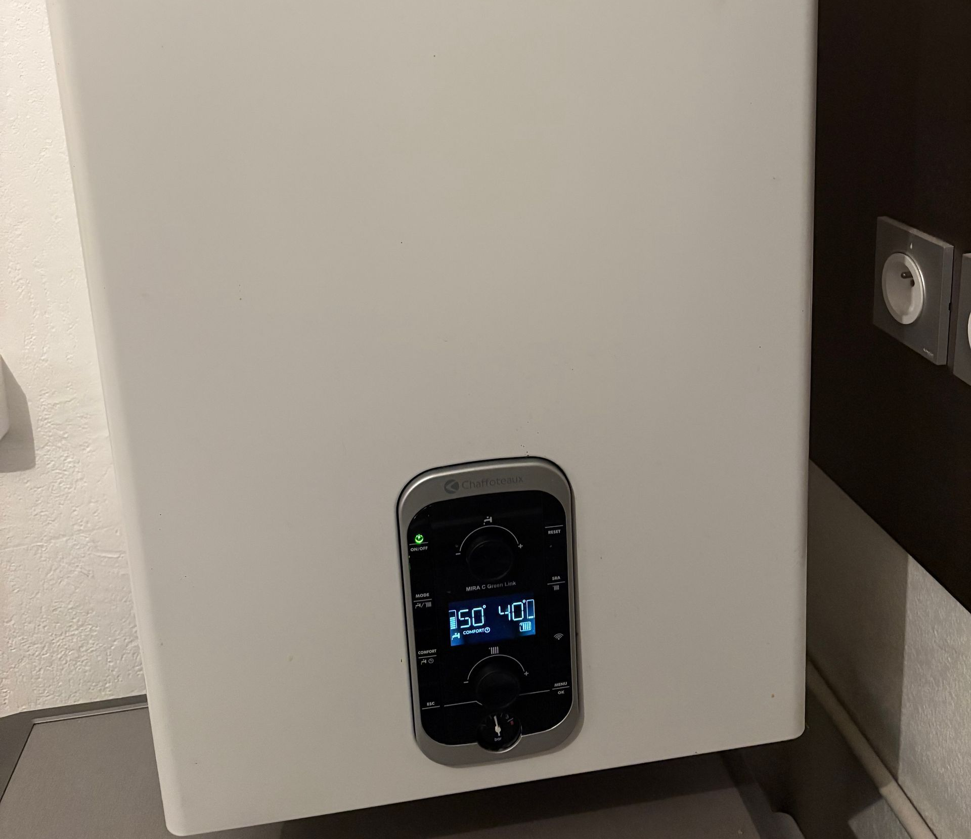 Chaudière murale blanche avec affichage numérique indiquant des chiffres et des flèches. Panneau de commande noir.