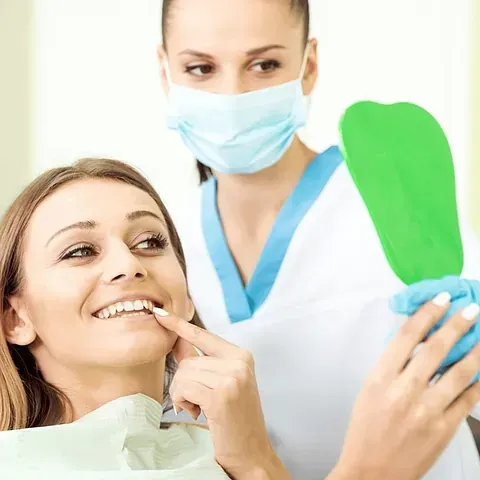 Una mujer sonríe mientras un dentista le mira los dientes.