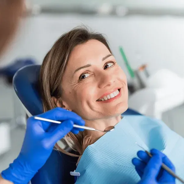 Una mujer sonríe mientras un dentista le examina los dientes.