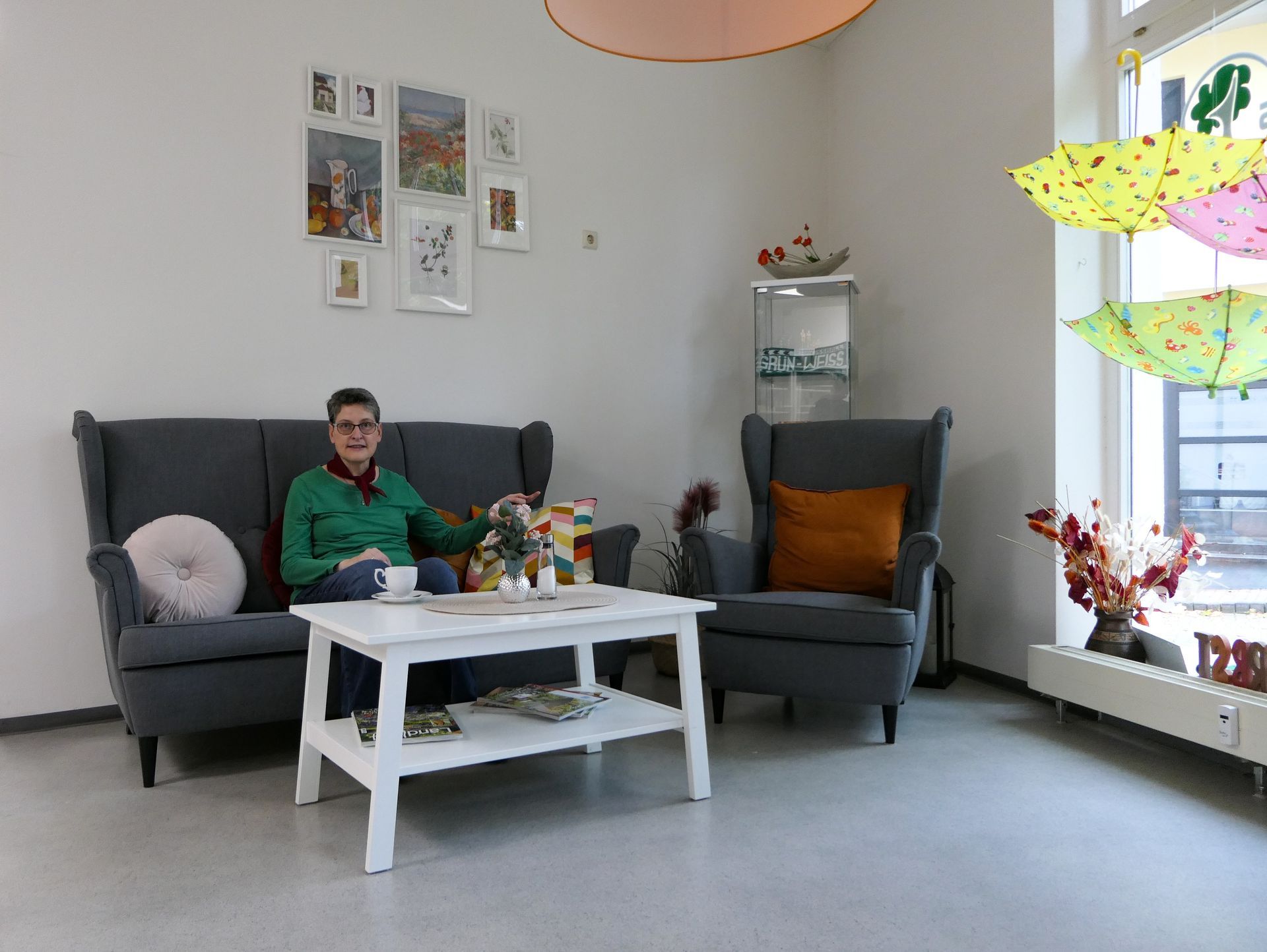 Kaffeestübchen: Dunkelgraue Couch und zwei Sessel mit braunen Kissen, Frau auf der Couch