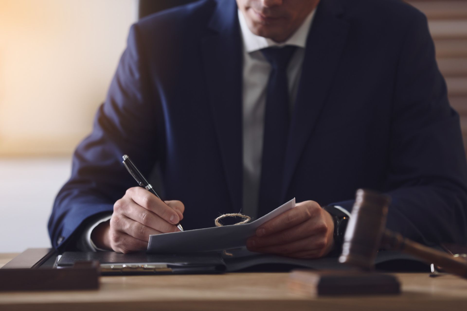 Un hombre con traje y corbata está sentado en un escritorio escribiendo en un trozo de papel.