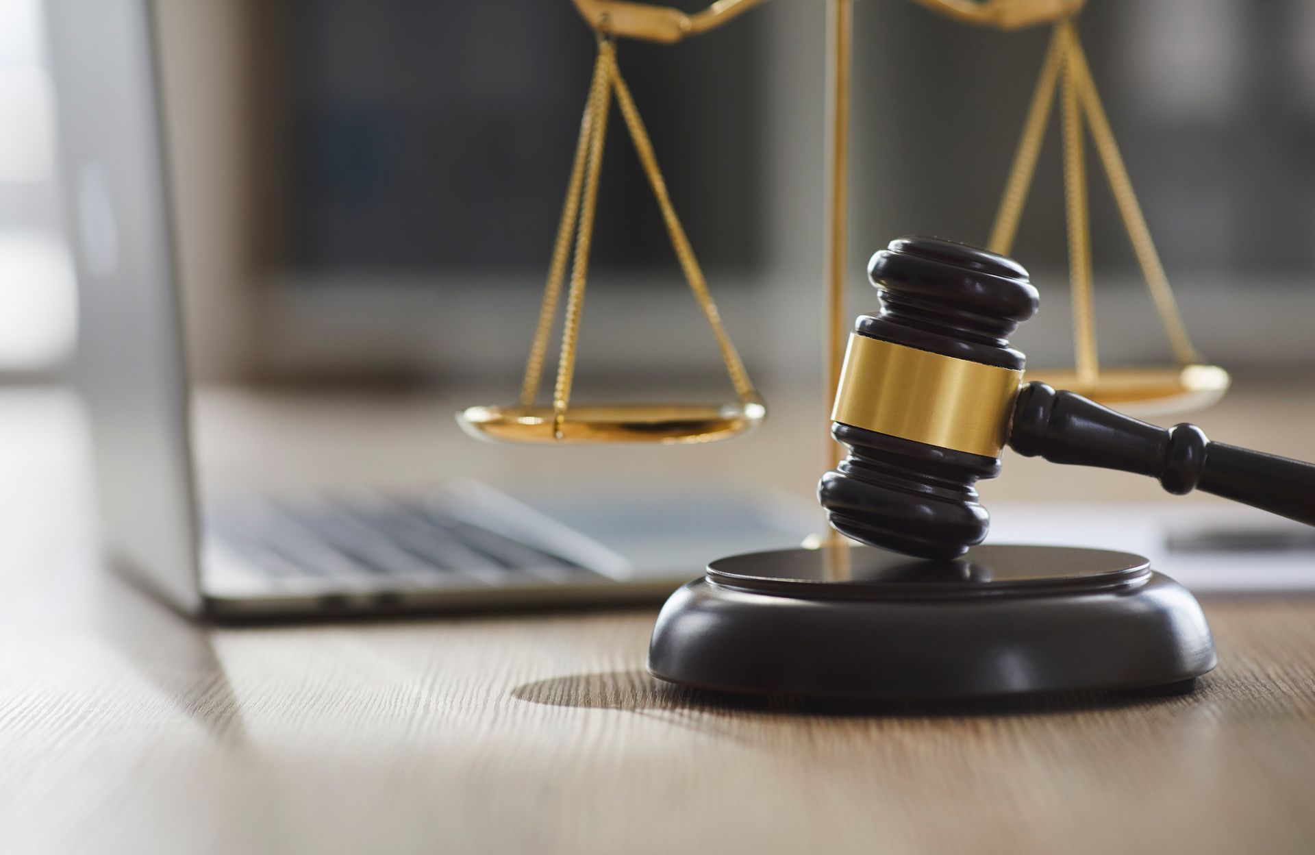 El mazo de un juez y la balanza de la justicia están sobre una mesa de madera frente a una computadora portátil.