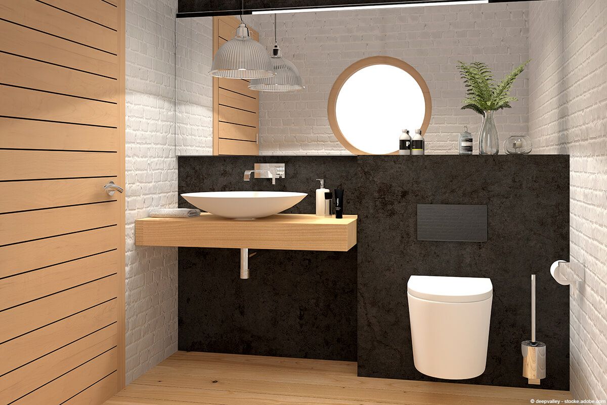 Modernes Badezimmer mit Holzakzenten, rundem Spiegel, weißem Waschbecken und Toilette vor einer dunklen Wand.