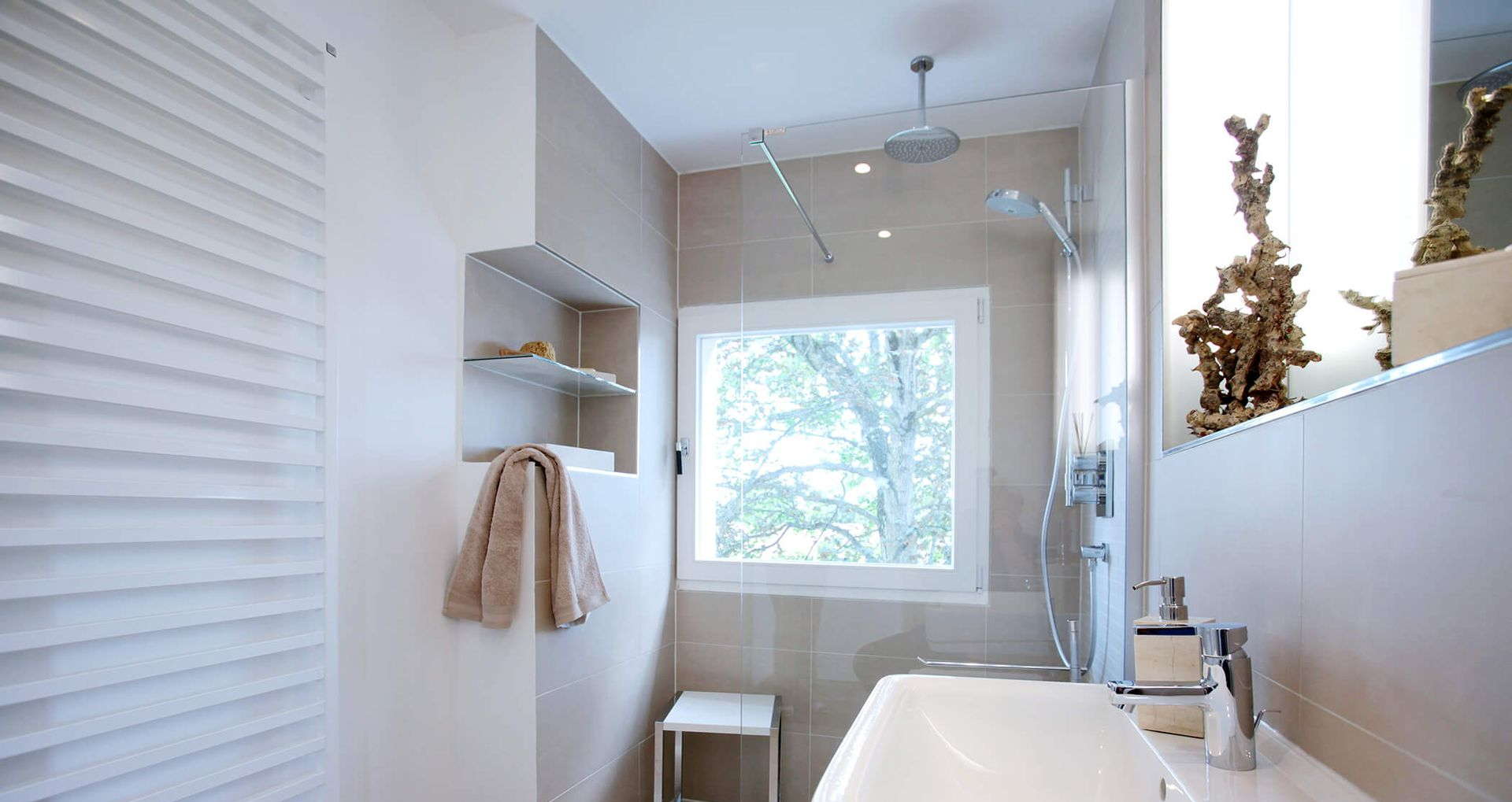 Eckdusche mit Glaswänden, Regenduschkopf, Handbrause und dunkelgrauem Boden vor hellgrauer Wand.