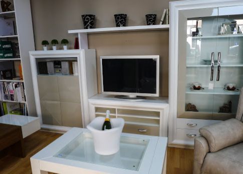 Sala de estar con muebles blancos, TV, mesa de cristal y cubeta de champán.