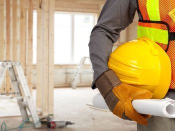 Un trabajador de la construcción sostiene un casco y un plano.