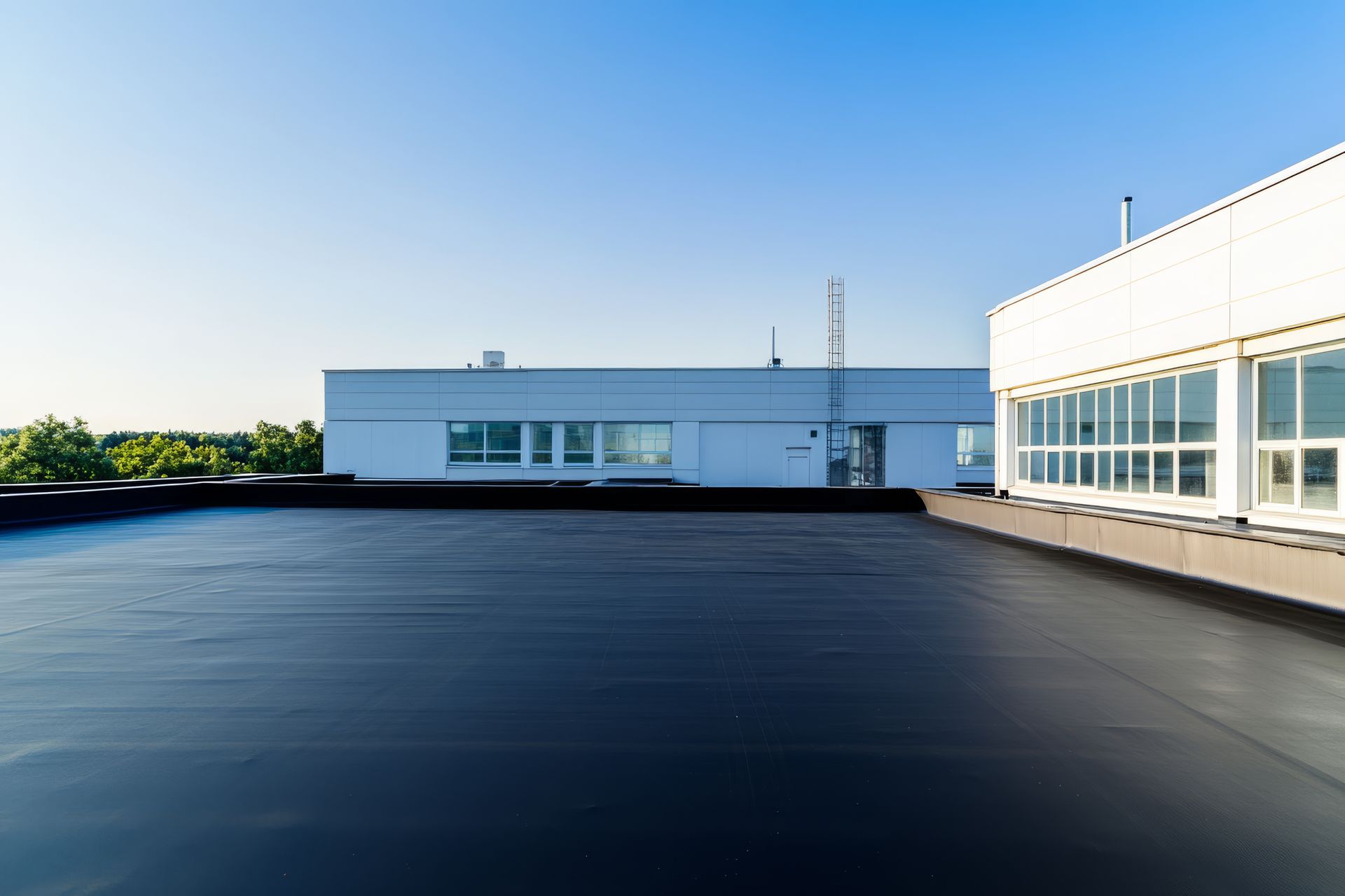 Un vaste toit plat noir avec des bâtiments commerciaux blancs en arrière-plan, sous un ciel bleu clair.